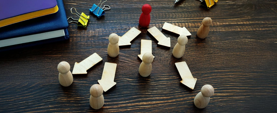 a small red wooden figure on a desk sends several white ones in various directions